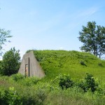 The grass-covered bunkers look like wrinkles in a vast green carpet. Placing earth on top of the bunkers served the dual purpose of maintaining a stable temperature inside for the TNT while camouflaging the sites from aerial view.